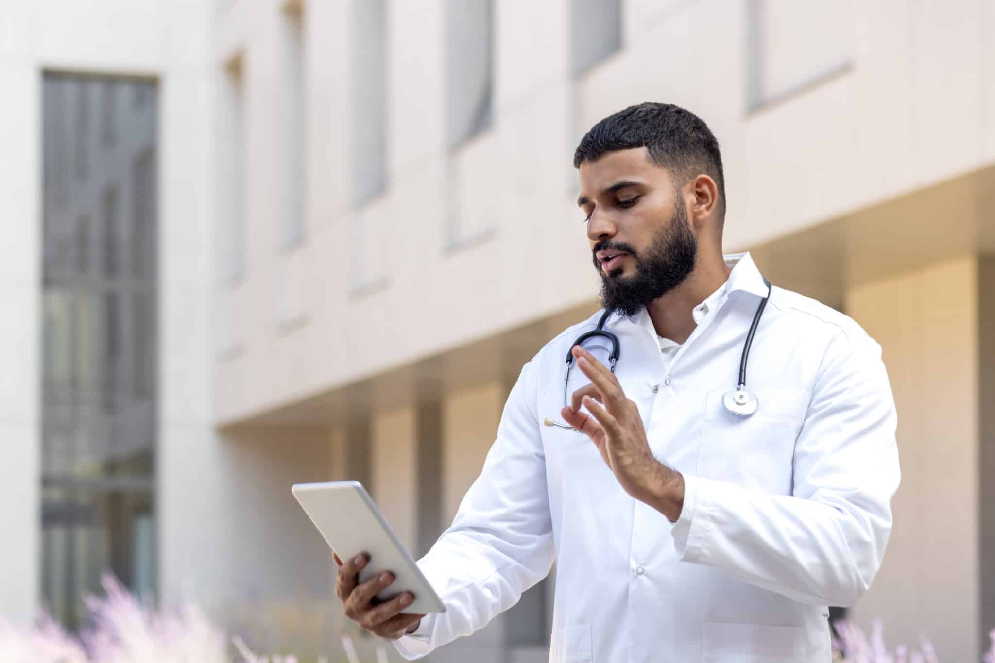 Physician in white coat dictating medical note via tablet, leveraging medical transcription services.