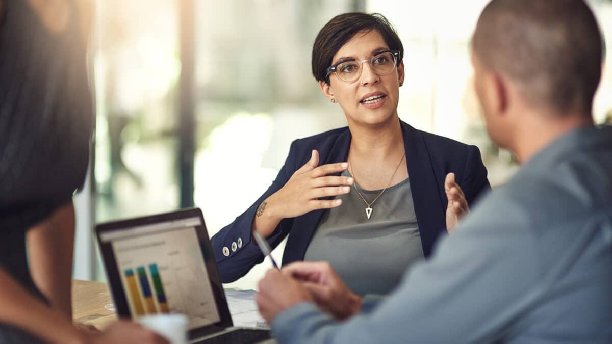 Accountant in a meeting uses laptop to show graphs; transcription plays a role in her data analysis.