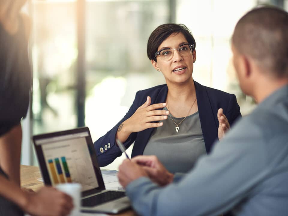 Accountant in a meeting uses laptop to show graphs; transcription plays a role in her data analysis.