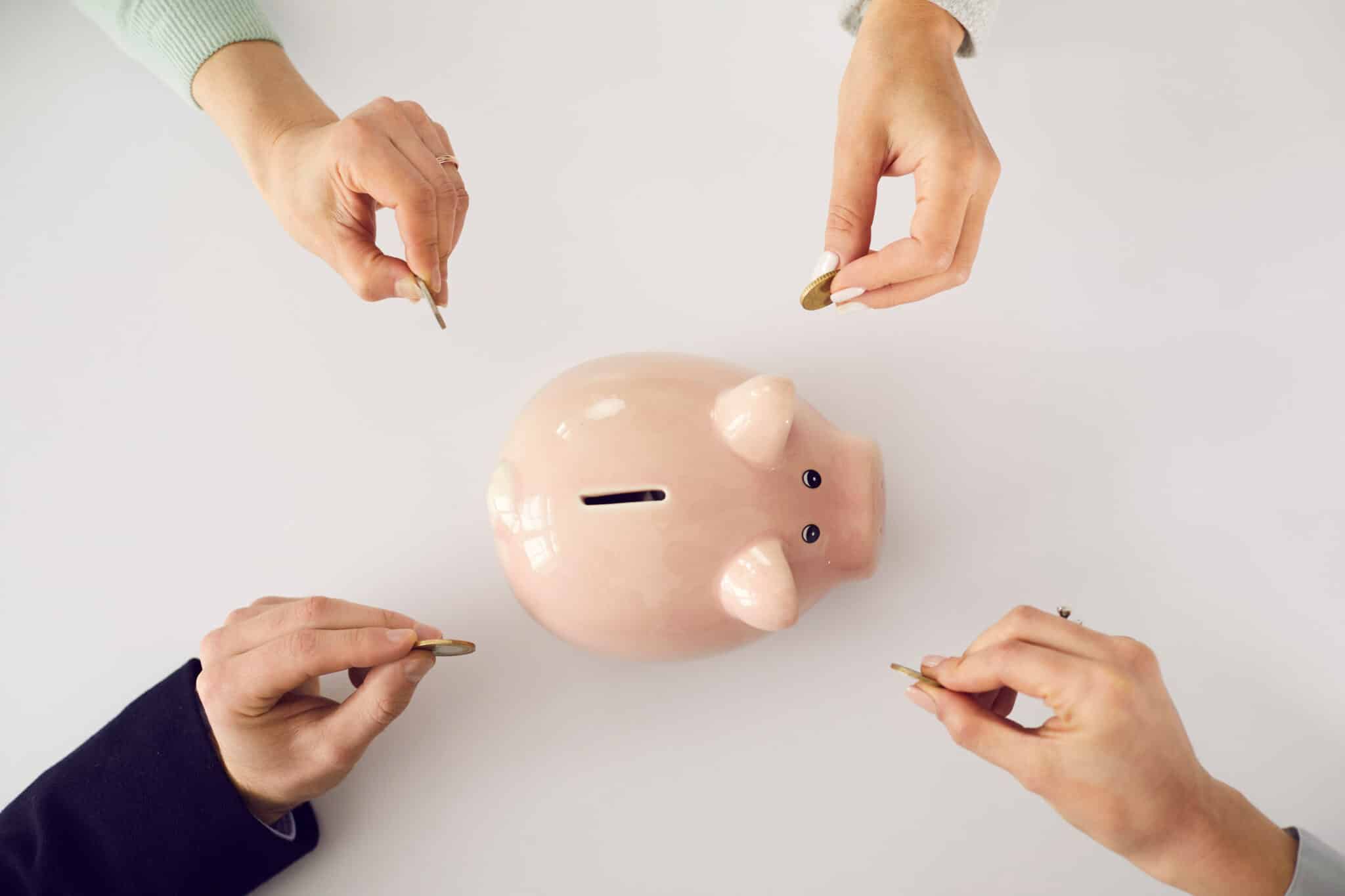Four hands add money to a pink piggy bank, symbolizing credit unions' commitment to member savings.
