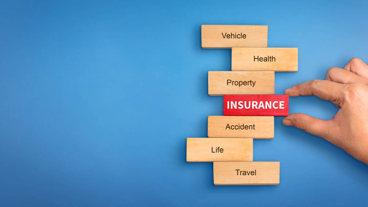 Hand holding a wooden 'Insurance' block, surrounded by blocks labeled with various insurance types.