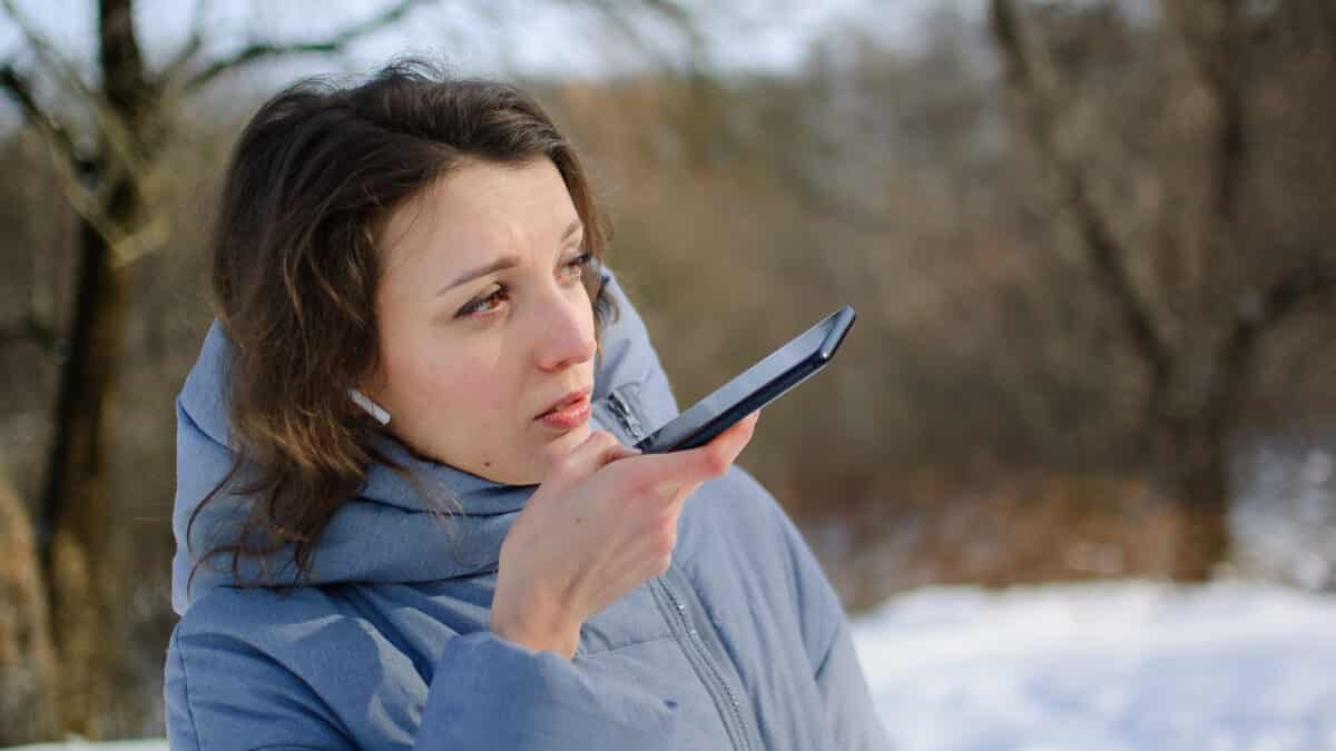 Insurance adjuster uses smartphone to dictate field notes for transcription outdoors at claim site.