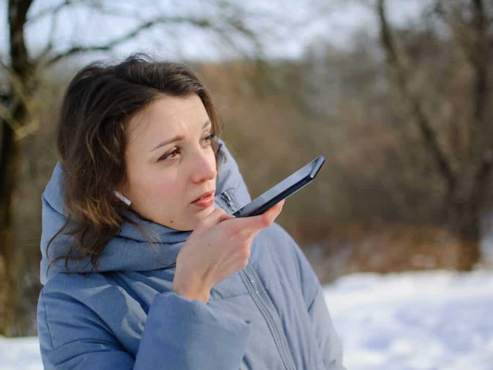 Insurance adjuster uses smartphone to dictate field notes for transcription outdoors at claim site.