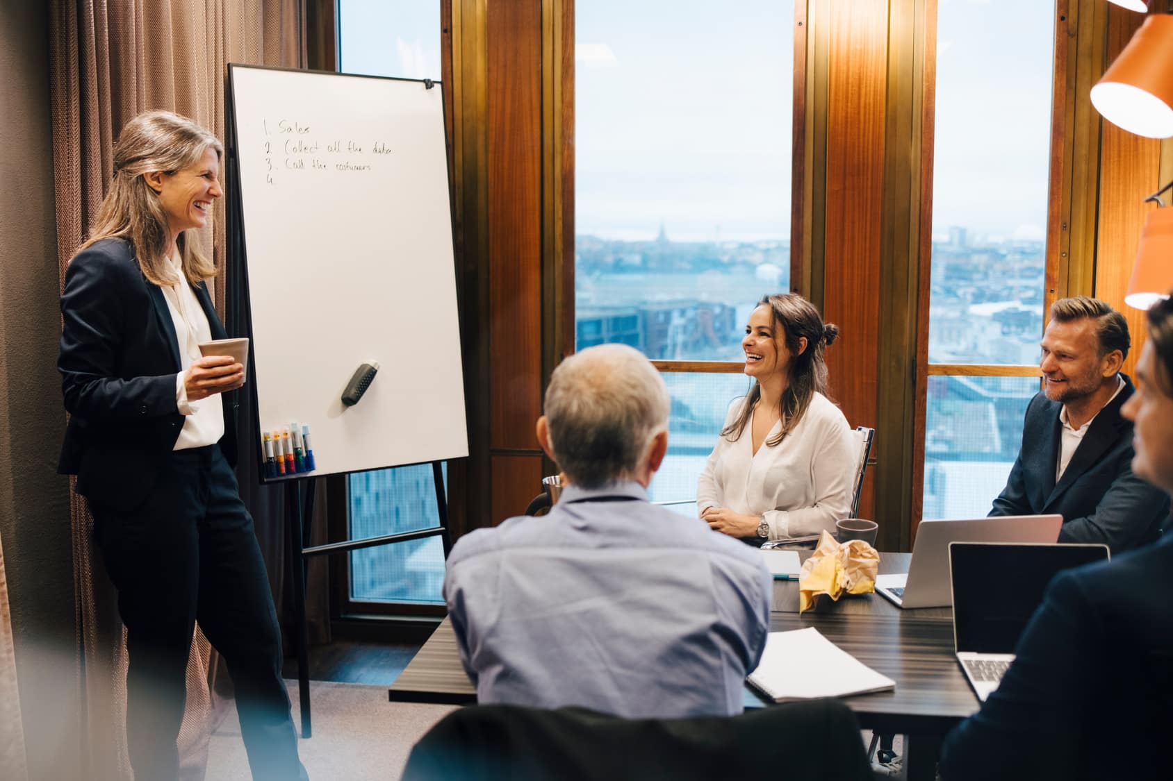 Smiling financier presents to colleagues in a boardroom; the meeting is recorded for transcription.