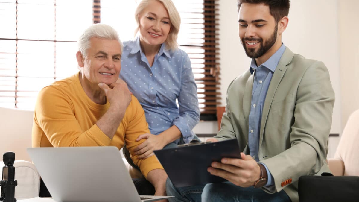 Male financial advisor with mature couple in office, recording their discussion for transcription.