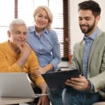 Male financial advisor with mature couple in office, recording their discussion for transcription.