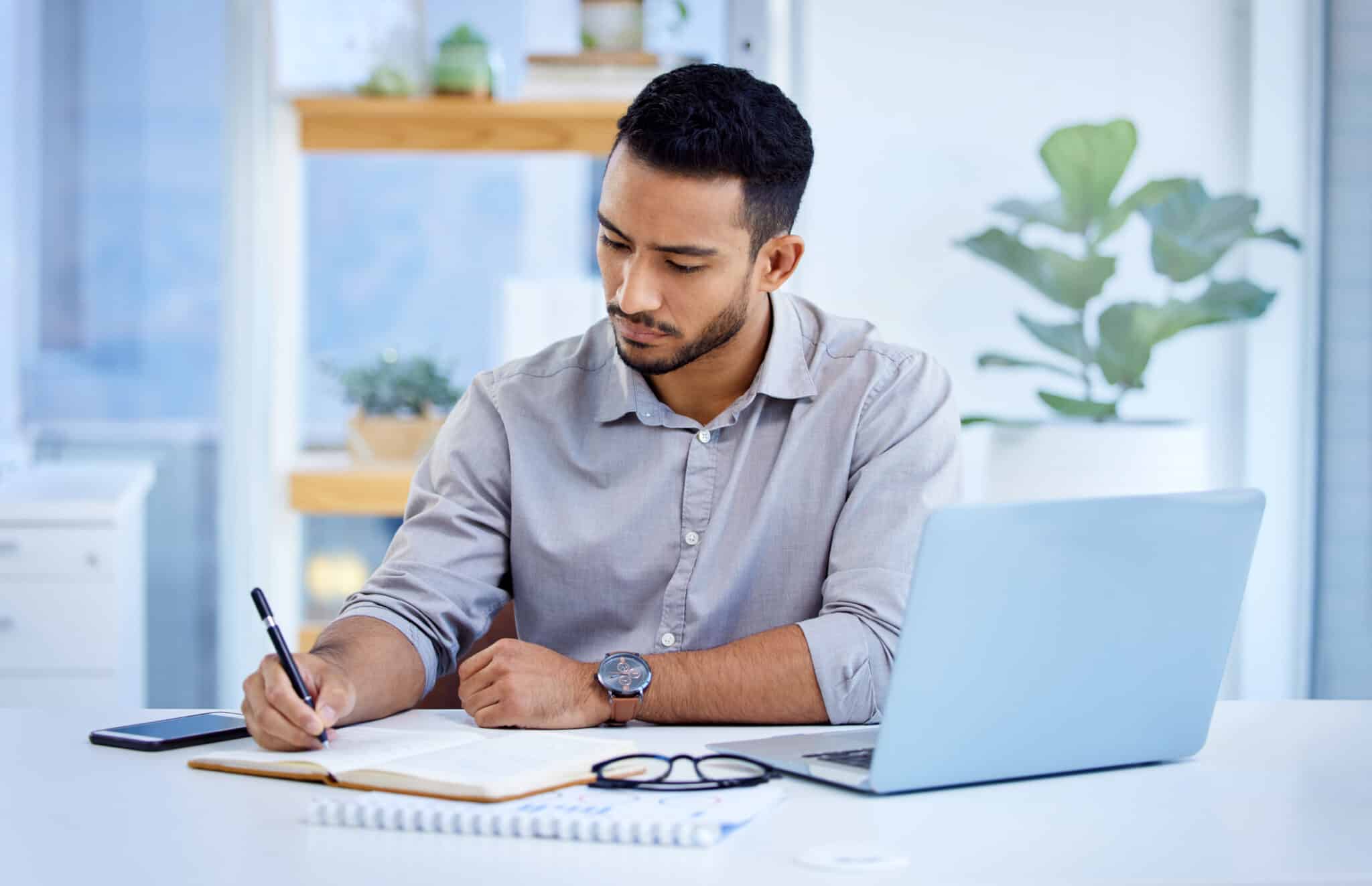 Young adjuster writes in his notebook and uses dictation services via his laptop for Symbility.