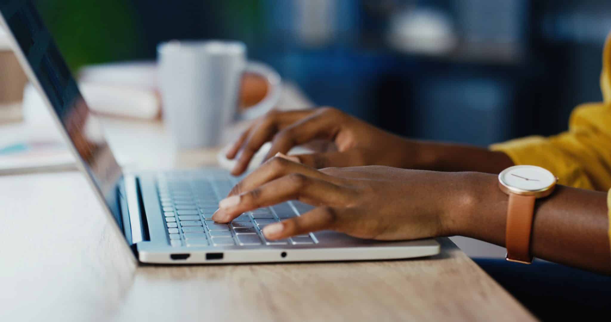 Woman efficiently typing on laptop keyboard at office desk, focusing on timely transcription work.