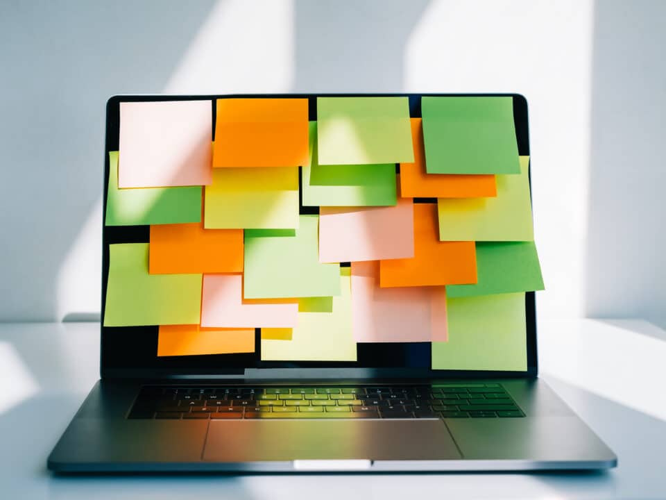 A laptop covered by many sticky notes symbolizes the stress of DIY video transcription efforts.