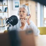 Senior female podcaster with headphones boosts her podcast using Athreon's transcription service.