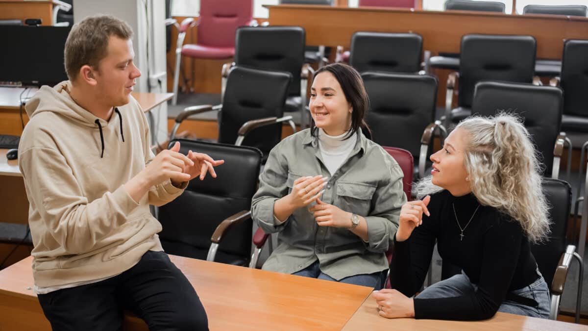 Three deaf students chat in sign language in a classroom, supported by Athreon's captioning service.