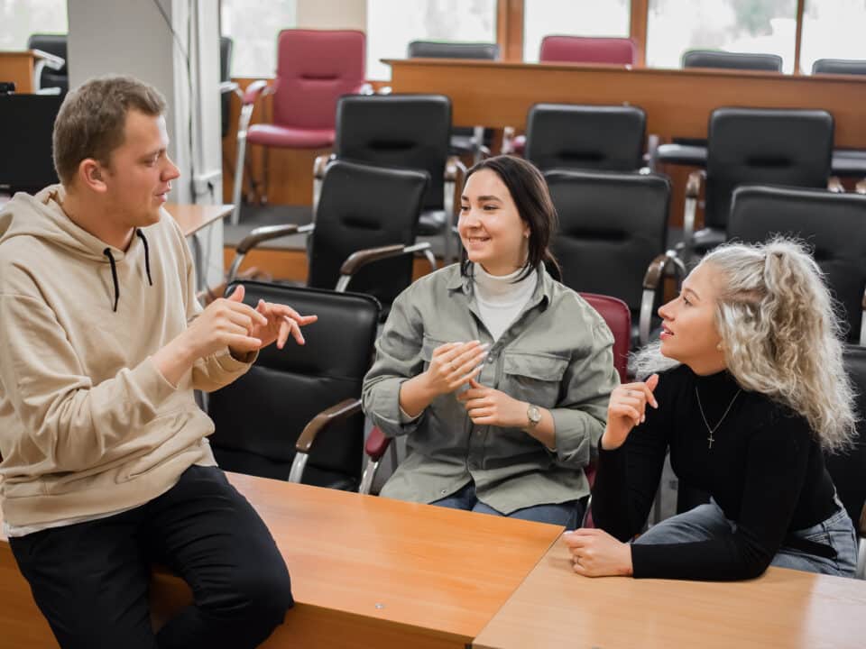 Three deaf students chat in sign language in a classroom, supported by Athreon's captioning service.