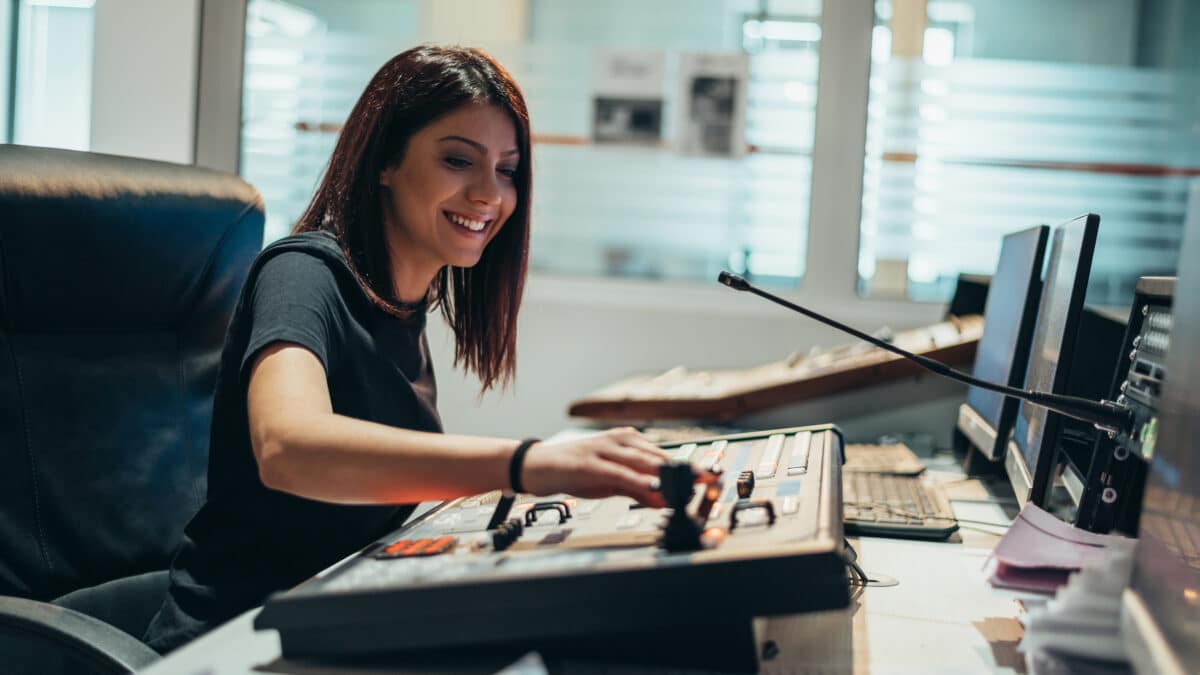 A woman operates equipment in a broadcast control room of a tv station using transcription services.