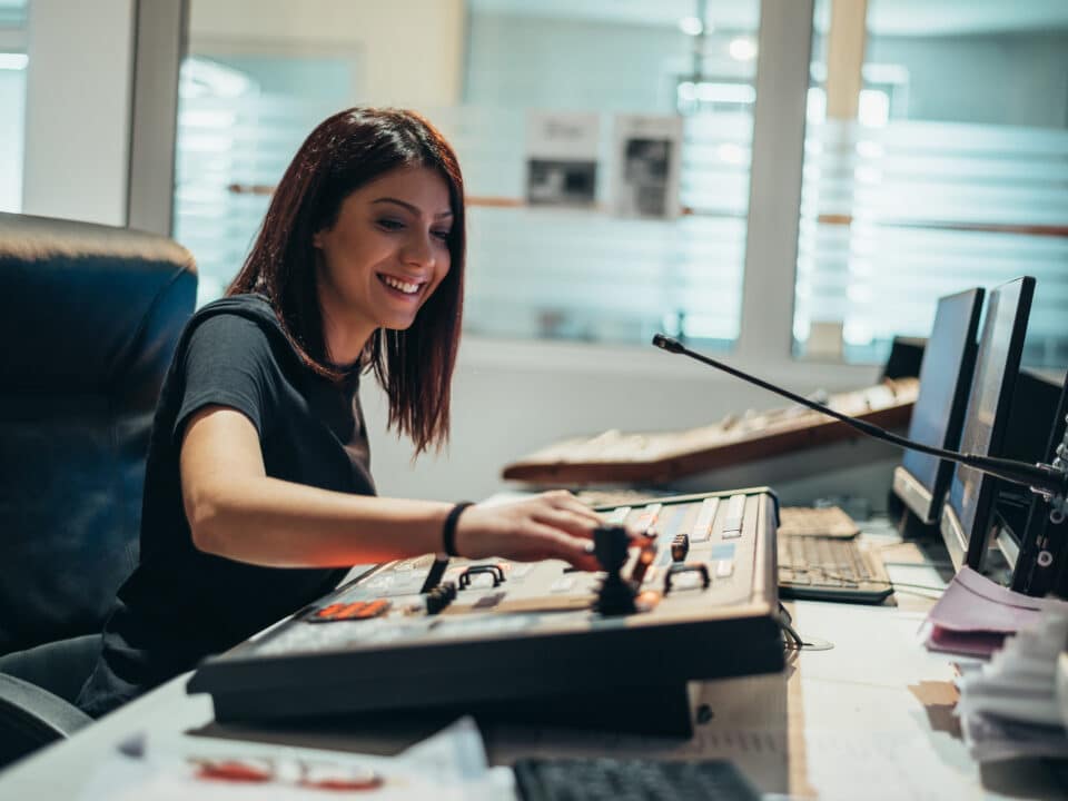 A woman operates equipment in a broadcast control room of a tv station using transcription services.