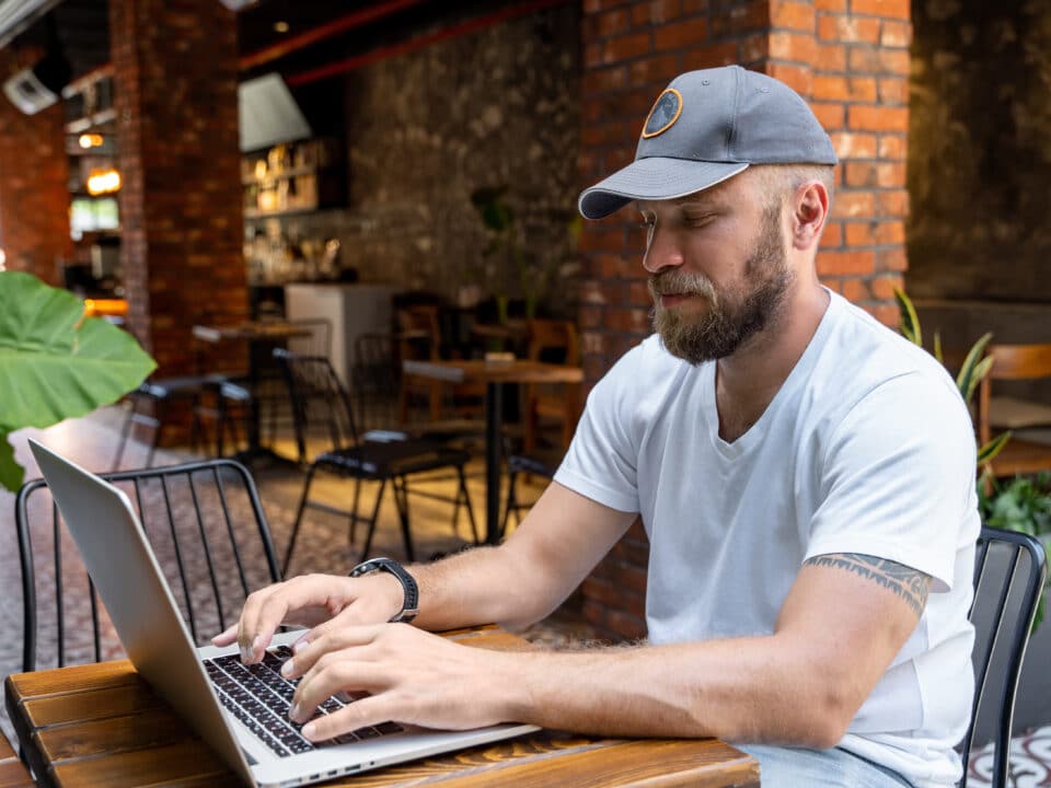 Man in casual clothes uses laptop in cafe, highlighting significance of cybersecurity in remote work