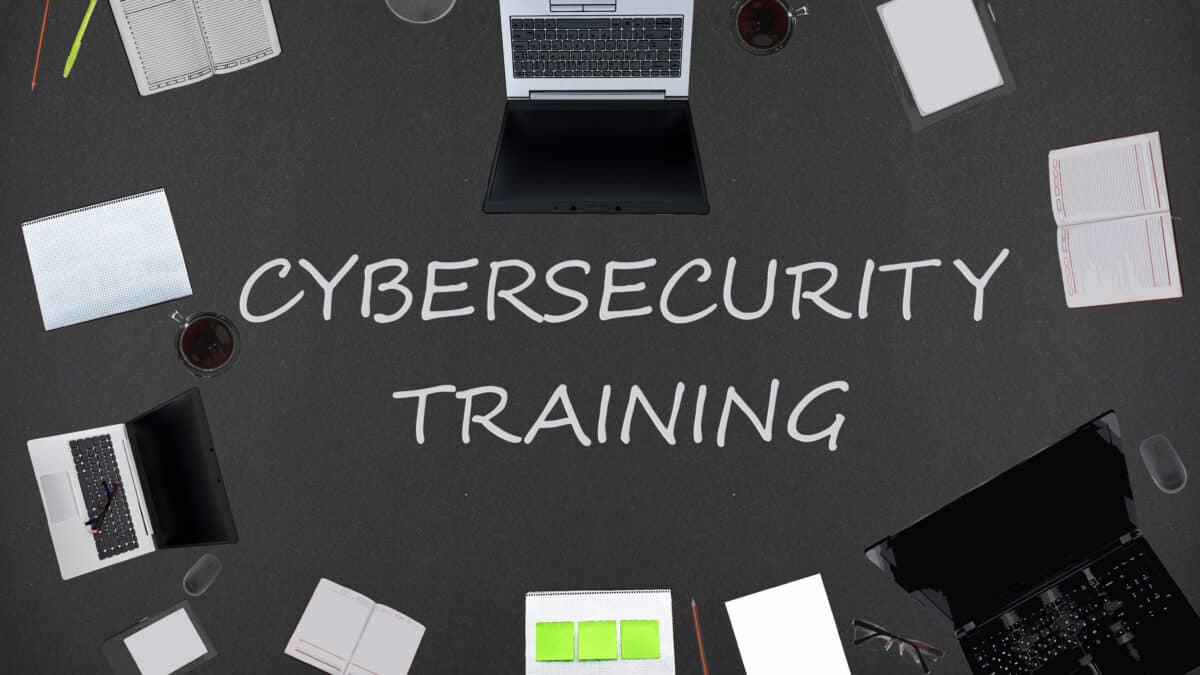 Top view of laptops, notepads, and coffee on a black background for employee cybersecurity training.