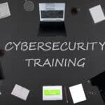 Top view of laptops, notepads, and coffee on a black background for employee cybersecurity training.