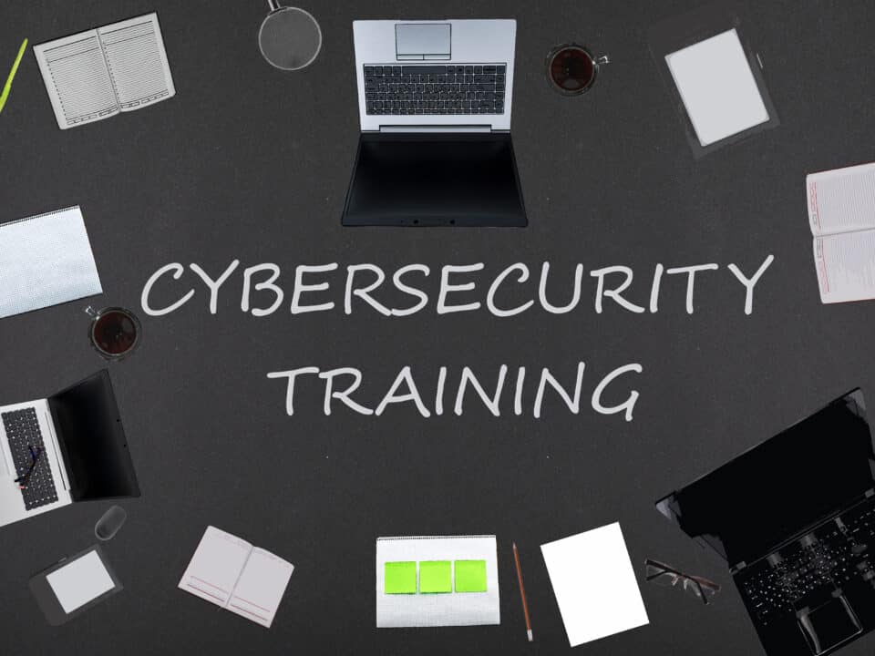 Top view of laptops, notepads, and coffee on a black background for employee cybersecurity training.